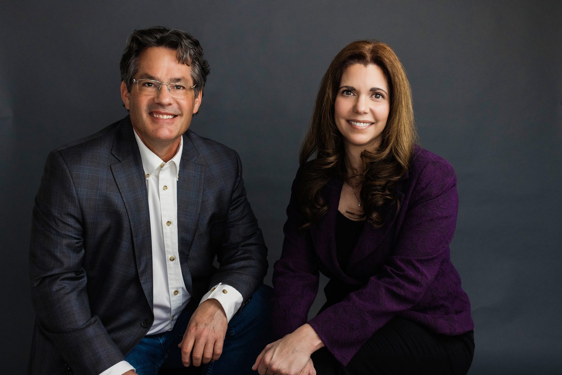 Dr. Jan Looman and Dr. Yolanda Fernandez seated together against a grey studio backdrop